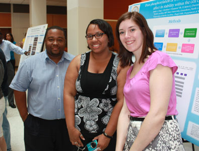 Three students pose in front of research posters