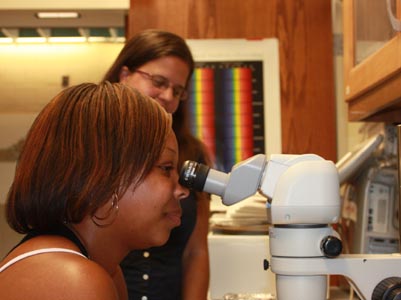 A black woman looking into a microscope